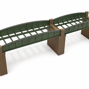 Può includere: Un ponte ferroviario modello con un arco in metallo verde e supporti in mattoni marroni. Il ponte ha un design a doppio binario ed è rialzato. Il ponte è una replica in miniatura di un ponte ferroviario.