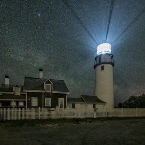 Faro de Cape Cod Highland bajo las estrellas: casa del farero y haz de luz del faro. Impresión del cielo nocturno.