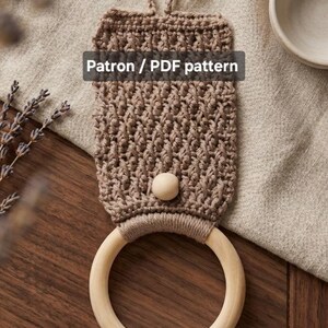 Peut inclure: Un porte-serviette en crochet marron avec une section supérieure rectangulaire texturée munie d'une boucle de suspension, une perle en bois clair et un anneau en bois circulaire lisse à la base. Le texte "Patron / PDF pattern" est visible.