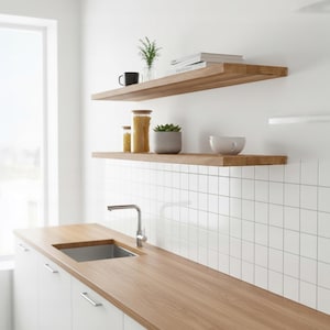 Könnte beinhalten: Zwei hellbraune, hölzerne Wandregale an einer weißen Wand über einer Küchenarbeitsplatte. Die Regale enthalten eine schwarze Tasse, eine Glasvase mit Grünpflanzen, Bücher, zwei Gläser mit Nudeln, einen grauen Sukkulententopf und eine weiße Schale.