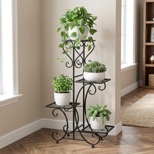 Peut inclure: Un support pour plantes en métal noir à quatre niveaux avec des détails en volutes. Le support contient quatre pots en céramique blanche avec diverses plantes vertes, dont un pothos retombant, une succulente et deux plantes feuillues.