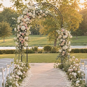 Könnte beinhalten: Ein schwarzer Metallbogen, verziert mit einem Arrangement aus weißen und blassrosa Rosen, Hortensien und grünem Eukalyptuslaub. Der Bogen steht über einem Steinweg, der von weißen Stühlen und niedrigen Blumenarrangements gesäumt ist.
