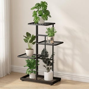 Può includere: Un supporto per piante a più livelli in metallo nero con cinque ripiani quadrati disposti ad altezze variabili. Il supporto ospita cinque piante in vaso, tra cui una grande monstera, un vaso in ceramica decorato e tre piante verdi.