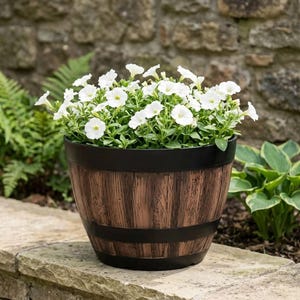 Puede incluir: Una maceta redonda con acabado de veta de madera marrón y bandas negras, llena de un denso grupo de pequeñas flores blancas con follaje verde. El recipiente tiene una forma cónica con un borde negro liso en la parte superior y una banda.