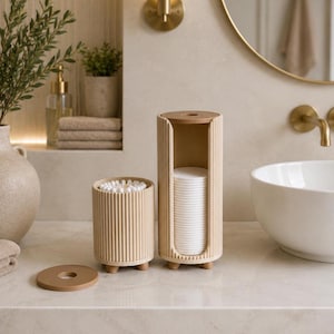 May include: A beige ribbed cylindrical cotton swab holder and a matching tall cotton pad dispenser with a vertical opening. Both containers feature small feet and a flat circular lid, with the cotton pad dispenser lid placed separately nearby.