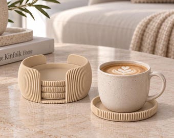 May include: A set of beige circular coasters with a vertical ribbed texture, stacked inside a matching cylindrical holder, alongside a speckled beige ceramic coffee mug resting on an identical ribbed coaster with latte art inside.
