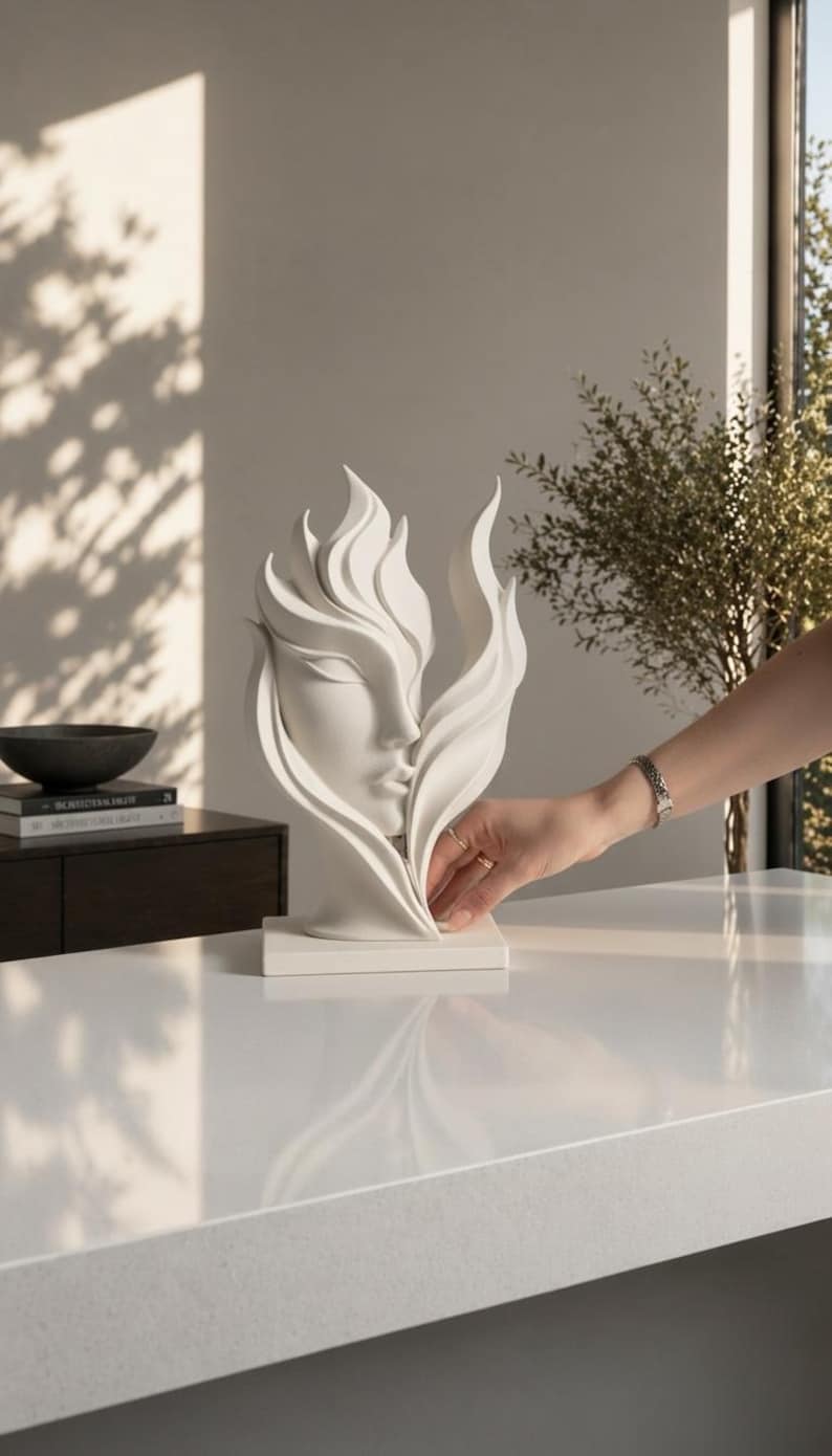 May include: A white sculpture of a face with flowing, flame-like shapes. The sculpture is on a white base and sits on a white surface. The sculpture is a decorative item.