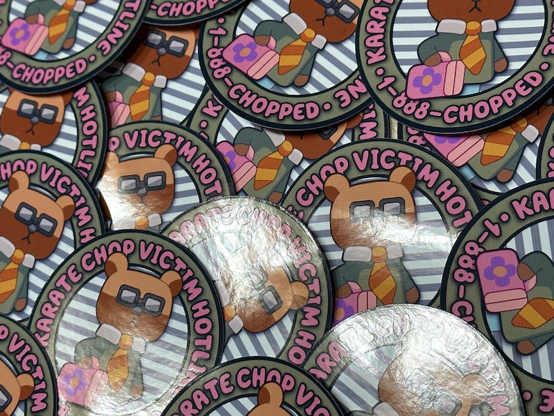 Puede incluir: Primer plano de varias pegatinas redondas con un oso de dibujos animados que lleva gafas y corbata. Las pegatinas tienen un fondo a rayas y el texto "KARATE CHOP VICTIM HOTLINE 1-888-CHOPPED" en rosa y blanco.