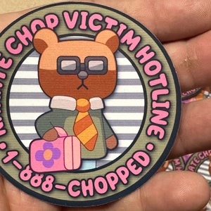 Puede incluir: Una pegatina redonda con un oso de dibujos animados que lleva gafas y corbata. La pegatina tiene el texto "KARATE CHOP VICTIM HOTLINE &bull; 1-888-CHOPPED" en letras rosas alrededor del borde.