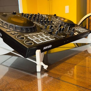 以下が含まれることがあります： 白いスタンドが付いた黒いDJミキサー。ミキサーの中央には大きなノブがあり、さまざまなボタンとノブがあります。ミキサーには「Pioneer DJ」と「Serato」の文字が見えます。