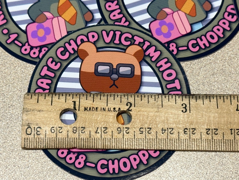 Puede incluir: Un oso marr&oacute;n con gafas sobre un fondo a rayas rosa y blanco. El oso sostiene una maleta rosa con una flor encima. El texto alrededor del oso dice "Rate Chop Victim Hot 888-Chopped".