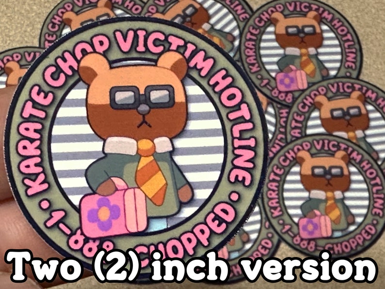 Puede incluir: Una pegatina redonda de 5 cm de di&aacute;metro con un oso marr&oacute;n de dibujos animados que lleva gafas y corbata. El oso sostiene una bolsa rosa con un dise&ntilde;o de flor. La pegatina tiene un fondo a rayas y el texto "KARATE CHOP VICTIM HOTLINE 1-888-CHOPPED." en letras rosa y negras.