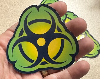 May include: A green and yellow biohazard symbol sticker with a black outline. The sticker is shaped like a triangle with three rounded points.