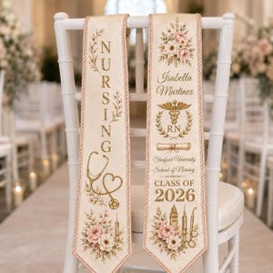 May include: Two cream-colored graduation stoles with pink trim and floral designs. One reads "NURSING" with a stethoscope graphic. The other displays a name, medical symbol, and "CLASS OF 2026".