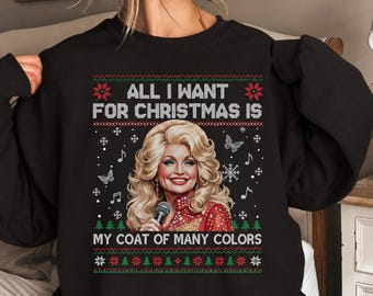 May include: A black long-sleeve sweatshirt featuring a graphic print of a blonde woman holding a microphone. The text reads ALL I WANT FOR CHRISTMAS IS MY COAT OF MANY COLORS. The design includes red and green holiday patterns with snowflakes.