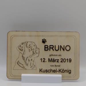 Könnte beinhalten: Holz-Gedenktafel für Haustiere mit dem Namen "BRUNO" in dunkler brauner Schrift graviert. Die Tafel enthält einen Pfotenabdruck, eine Hundeillustration und das Geburtsdatum "12. März 2019". Die Tafel wird von einem weißen Ständer getragen.