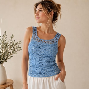 May include: A light blue sleeveless crochet tank top featuring a wide scoop neckline with an openwork lattice pattern at the shoulders and a dense vertical stitch pattern throughout the main body, paired with a plain white skirt.
