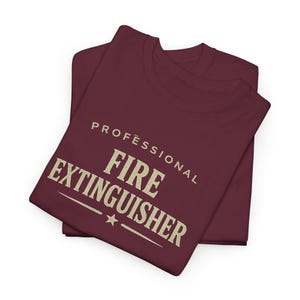 May include: A maroon t-shirt featuring the beige text "PROFESSIONAL FIRE EXTINGUISHER" printed in a bold, serif font across the chest. The design includes a small star centered below the word "FIRE" and horizontal lines flanking the text.