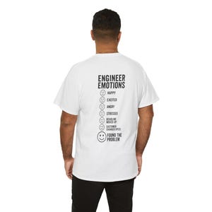 May include: A white short-sleeved t-shirt featuring black text on the back that reads ENGINEER EMOTIONS followed by a list of facial expressions labeled Happy, Excited, Angry, Stressed, Deadline Moved Up, Customer Changed Specs, and Found The Problem.