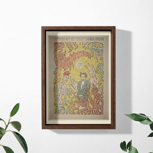 May include: A framed art print featuring a James Ensor exhibition poster with a central figure surrounded by fantastical, demonic creatures in yellow, red, and green ink. The text at the top reads "SALON DES CENT EXPOSITION JAMES ENSOR".