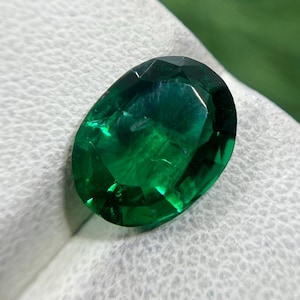 May include: A loose, oval-cut gemstone with a deep, vibrant emerald green color. The stone features a faceted surface that reflects light, creating a brilliant, multi-dimensional appearance with clear internal clarity and sharp edges.
