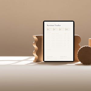 Pu&ograve; includere: Un tablet nero che mostra un documento "Revision Tracker", sostenuto da forme geometriche in legno. Le forme includono una forma ondulata, un cilindro e un pezzo circolare. Lo sfondo &egrave; beige neutro.