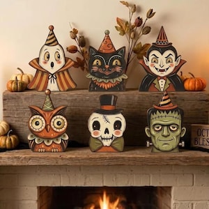 Könnte beinhalten: Sechs dekorative Holzausschnitte mit Halloween-Figuren: ein Geist im gestreiften Umhang, eine schwarze Katze, ein Vampir, eine Eule, ein Totenkopf mit Zylinder und ein grünes Monster. Jede Figur trägt einen Partyhut und zeigt detaillierte Zeichnungen.