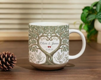 Könnte beinhalten: Ein weißer Keramikbecher mit Henkel, bedruckt mit einer Illustration eines Baumes, dessen ineinander verschlungene Äste eine Herzform bilden. Das Design zeigt zwei weiße Tauben, den Text Olivia & James, zwei kleine rote Herzen und das Datum 11.08.25.
