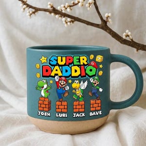 Peut inclure: Mug en céramique bleu sarcelle avec une base beige, avec le texte "SUPER DADDIO" et des personnages de dessins animés. La tasse a une anse et les noms "JOSH", "LURI", "JACK" et "DAVE" en dessous.
