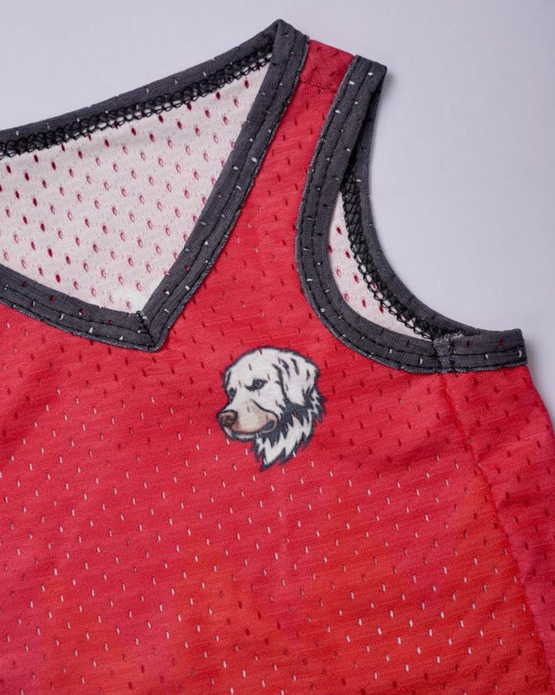 May include: A red sleeveless mesh tank top featuring a V-neckline with dark gray trim. The garment is constructed from a perforated athletic fabric and displays a small, detailed graphic illustration of a white dog head on the front chest area.
