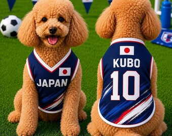 Könnte beinhalten: Ein beigefarbener Pudel trägt ein marineblaues Hunde-Trikot mit weißem Rand. Auf der Vorderseite steht JAPAN und die japanische Flagge. Auf der Rückseite sind der Name KUBO, die Nummer 10, die japanische Flagge und blau-weiß-rote Pinselstriche.
