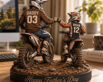 Könnte beinhalten: Detaillierte Figur eines Vaters und Kindes auf Dirtbikes, die sich abklatschen. Das Trikot des Vaters trägt die Aufschrift "DADDY 03", das des Kindes "BRIAN 12". Die Basis ist mit "Happy Father's Day" beschriftet. Die Motorräder sind orange und weiß.