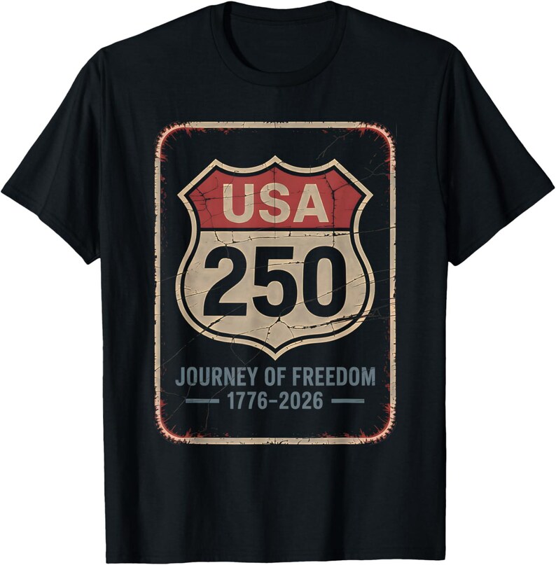 以下が含まれることがあります： 黒いTシャツ。USA 250とJourney of Freedom 1776-2026と書かれた、使い古された道路標識のデザイン。赤、ベージュ、黒の色使いで、ヴィンテージ感を醸し出しています。