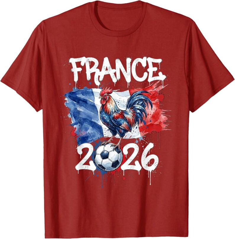 Op de afbeelding: Rood T-shirt met een aquarelontwerp. Het woord "FRANCE" staat in het wit boven een haan die op een voetbal staat. De Franse vlag staat op de achtergrond en het nummer "2026" staat eronder.