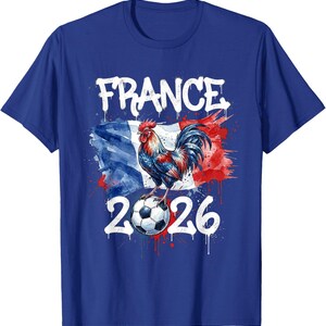 Op de afbeelding: Koning blauw t-shirt met een afbeelding van een haan op een voetbal, tegen de Franse vlag. Het woord "FRANCE" staat boven de haan en het nummer "2026" eronder. Het ontwerp heeft een distressed aquareleffect.