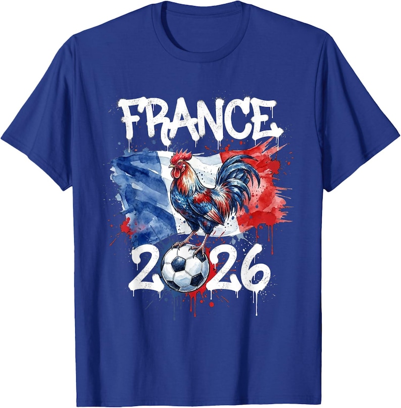 Op de afbeelding: Koning blauw t-shirt met een afbeelding van een haan op een voetbal, tegen de Franse vlag. Het woord "FRANCE" staat boven de haan en het nummer "2026" eronder. Het ontwerp heeft een distressed aquareleffect.
