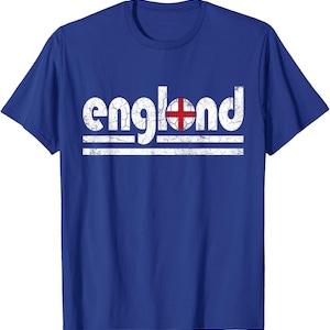 以下が含まれることがあります： 青いTシャツ。白の文字で「england」と書かれており、文字はかすれています。「o」の文字は、白い背景に赤い十字が入ったサッカーボールのデザインに置き換えられています。単語の下には2本の白い水平線があります。