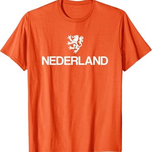 May include: Orange t-shirt with the word "NEDERLAND" in white block letters. Above the word is a white heraldic lion emblem. The shirt has short sleeves and a crew neck.