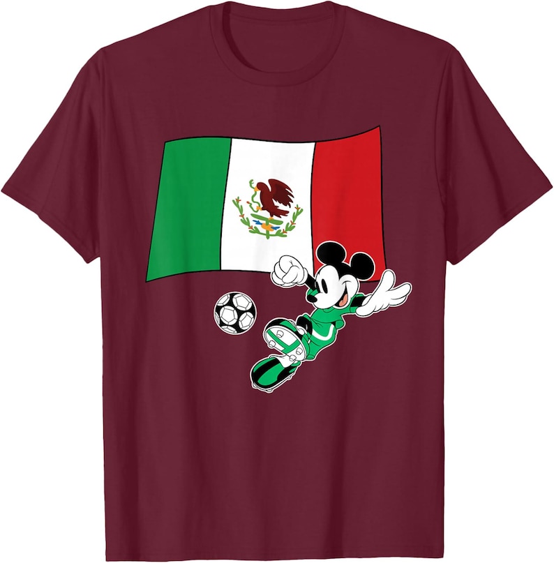 May include: Burgundy t-shirt featuring a graphic of Mickey Mouse in a green soccer uniform kicking a soccer ball. Behind Mickey is the Mexican flag. The design is centered on the front of the shirt.