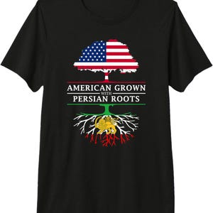 Pode incluir: Camiseta preta com um desenho de árvore. A copa da árvore é a bandeira americana e as raízes exibem a bandeira persa. O texto diz "AMERICAN GROWN with PERSIAN ROOTS".