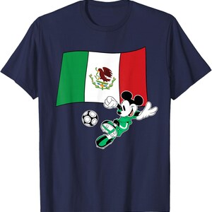 May include: Navy blue t-shirt featuring a graphic of Mickey Mouse in a green soccer uniform kicking a soccer ball. The Mexican flag is behind Mickey. The shirt is a crew neck.