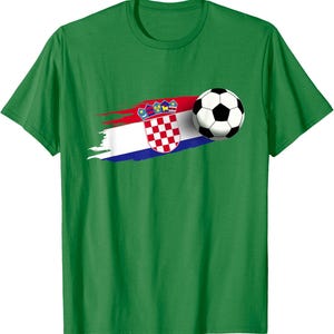 K&ouml;nnte beinhalten: Gr&uuml;nes T-Shirt mit einem Fu&szlig;ball und einem stilisierten kroatischen Flaggen-Design. Das Flaggen-Design enth&auml;lt das kroatische Wappen und einen rot-wei&szlig;-blauen Pinselstrich-Effekt. Der Fu&szlig;ball ist schwarz und wei&szlig;.