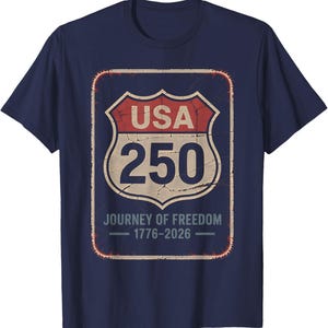 以下が含まれることがあります： ネイビーブルーのTシャツ。USA 250と「Journey of Freedom 1776-2026」と書かれた、使い古された道路標識のグラフィック。デザインは赤、ベージュ、白です。