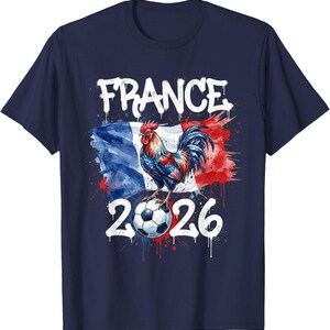 Op de afbeelding: Marineblauw T-shirt met een aquarelontwerp. Het toont het woord "FRANCE", een haan op een voetbal en het nummer "2026". Het ontwerp bevat de kleuren van de Franse vlag.