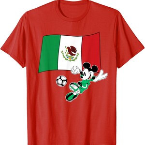 May include: Red t-shirt featuring a graphic of Mickey Mouse playing soccer in a green uniform. The Mexican flag is in the background, and a soccer ball is in front of Mickey. The shirt is made of a soft material.