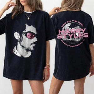 May include: Black t-shirt featuring a black and white graphic of a man wearing pink sunglasses. The front of the shirt displays the image, while the back has a disco ball design with the text "Kiss All The Time, Harry Styles, Disco, Occasionally."
