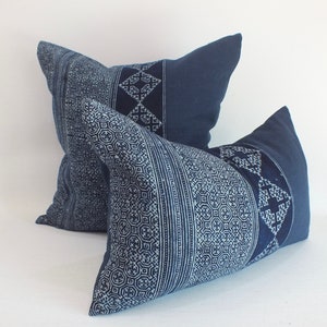 Puede incluir: Dos almohadas de tiro azul índigo con patrones geométricos blancos. Las almohadas están hechas de una tela suave y texturizada y tienen un aspecto ligeramente desgastado.