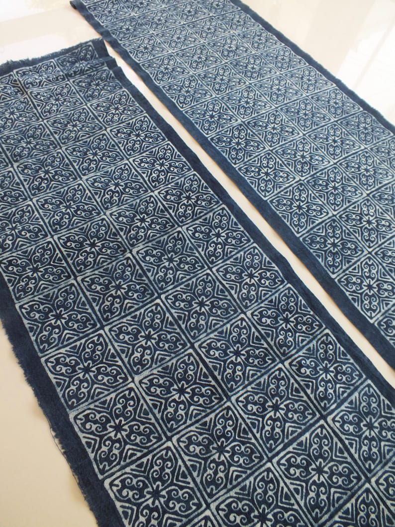 May include: Two indigo blue fabric table runners with a white geometric pattern. The pattern is a repeating square design with a floral motif.
