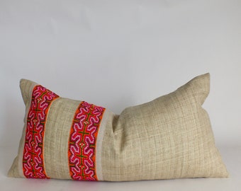 May include: A long, rectangular pillow with a beige linen cover. The pillow has a band of colorful embroidery in shades of pink, orange, and green running down the center.