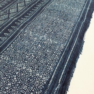 May include: A long, narrow piece of indigo-dyed fabric with a white geometric pattern. The fabric has a frayed edge and is folded in half.